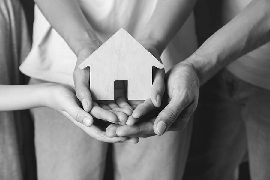 Familie hält ein kleines Holzhaus gemeinsam in den Händen